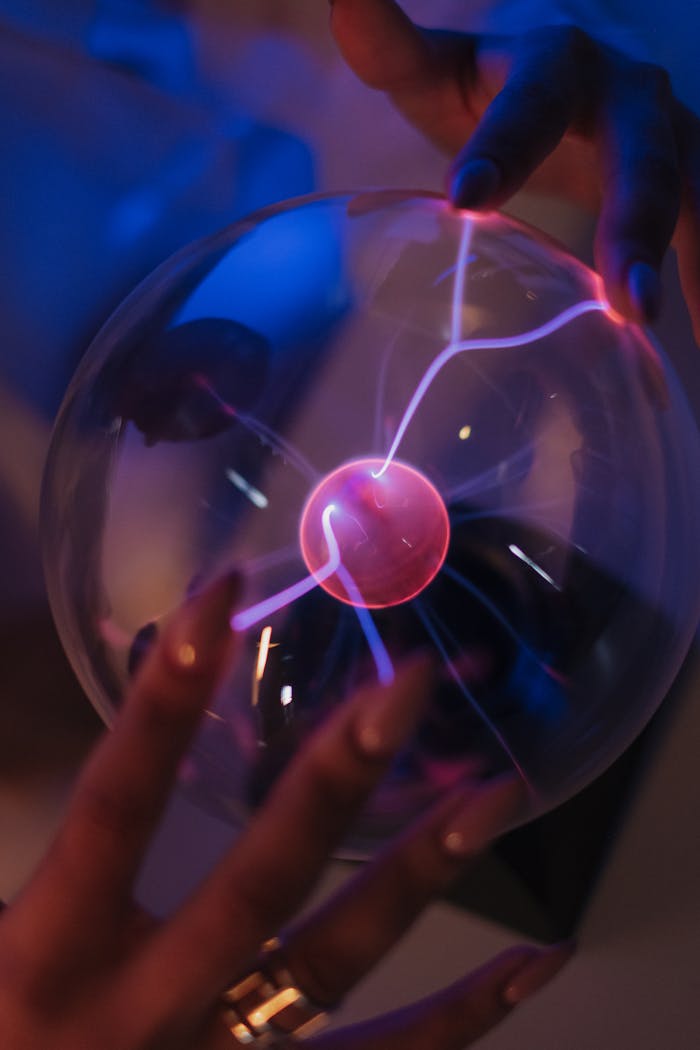 Close-up of adult hands interacting with a glowing plasma ball.
