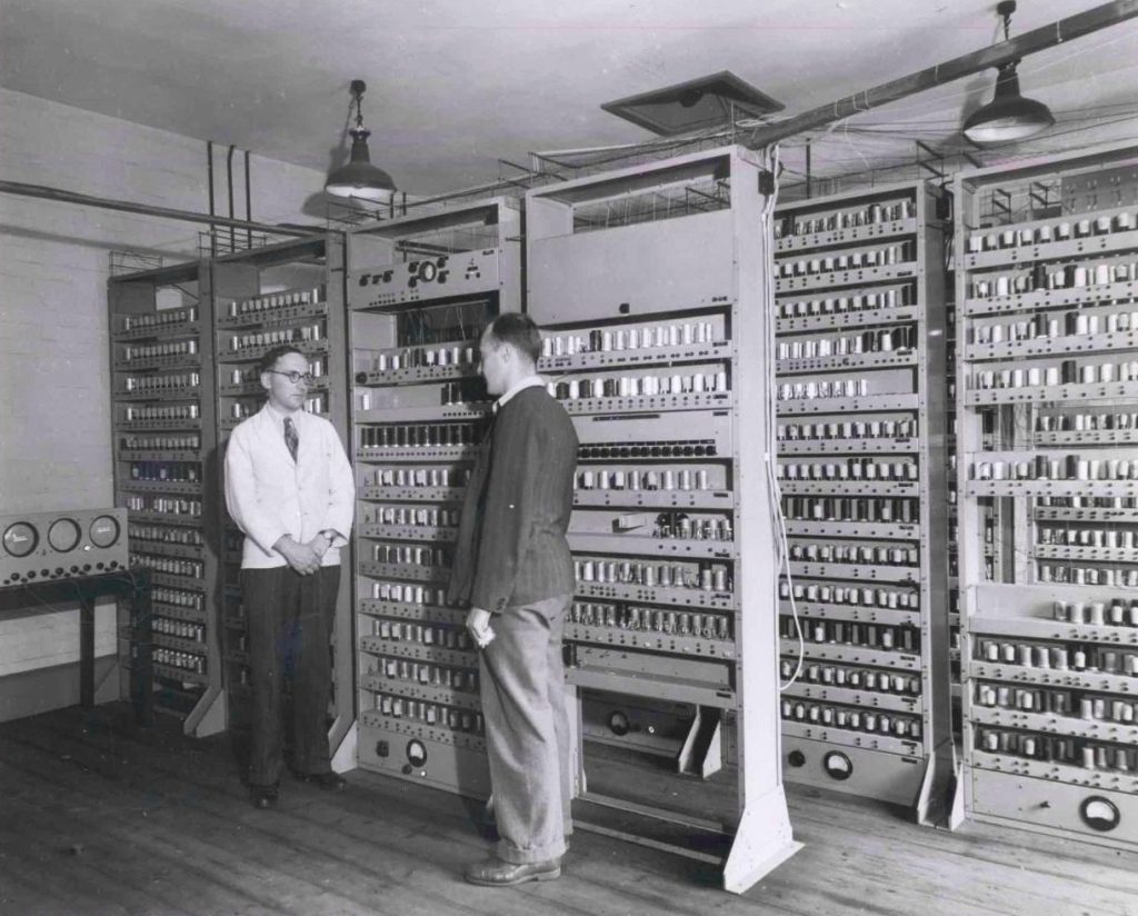 موریس ویلکس در کنار کامپیوتر EDSAC در آزمایشگاه ریاضیات دانشگاه کمبریج