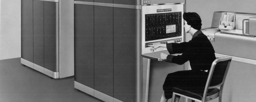 زن اپراتور پشت کنسول IBM 650 با پنل چراغهای چشمکزن و واحد خواندن/پانچ کارت در کنار آن